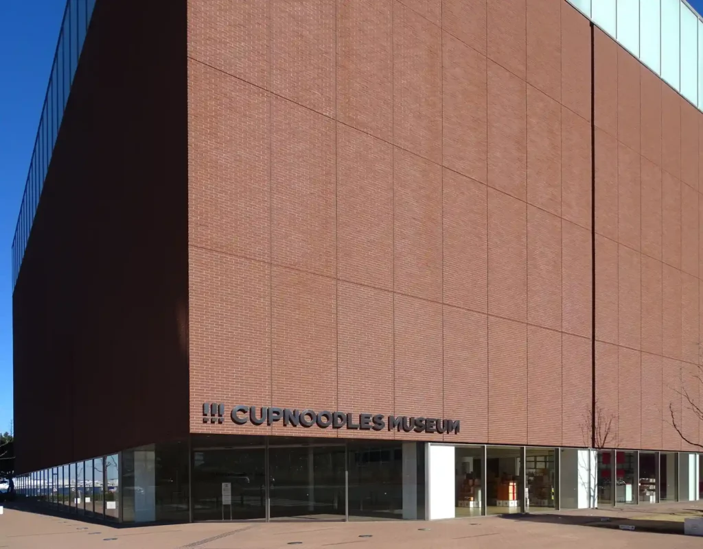 Exterior view of the modern brick building of the Cup Noodles Museum in Yokohama under a clear blue sky.