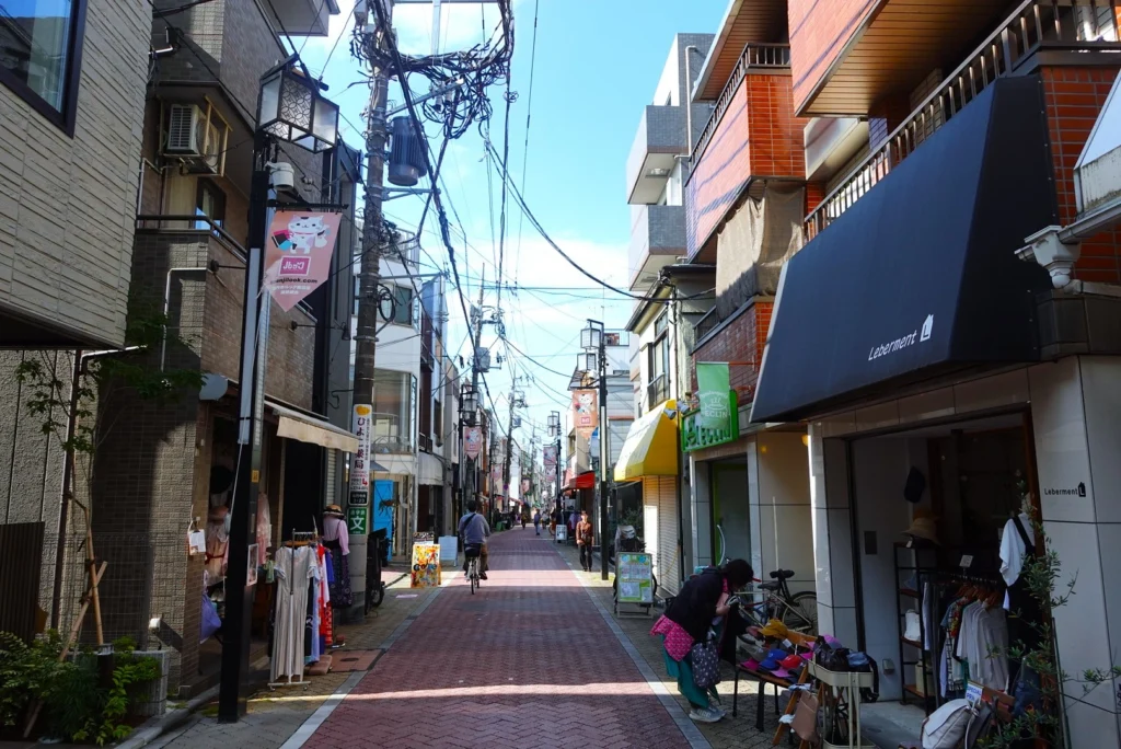A narrow brick-paved alleyway on Look Shopping Street in Koenji, featuring overhead power lines, pedestrians, and small independent vintage clothing boutiques.