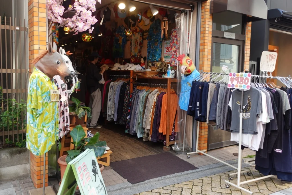 Colorful storefront of a Koenji thrift store, featuring vintage clothing on outdoor racks and quirky mannequins wearing animal masks.