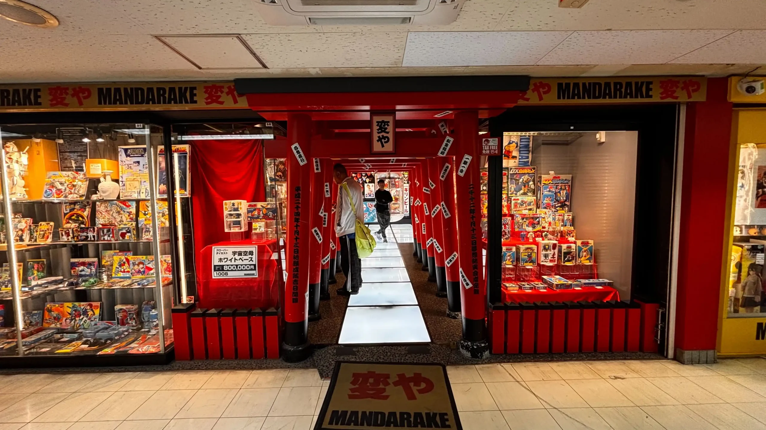 The red torii gate entrance of the Mandarake Henya store inside Nakano Broadway, flanked by glass display cases filled with vintage action figures and retro Japanese toys.