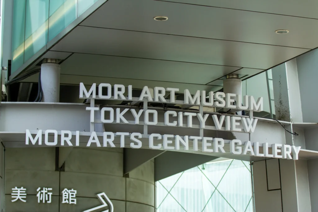 Overhead white entrance sign for the Mori Art Museum, Tokyo City View, and Mori Arts Center Gallery located at Roppongi Hills.