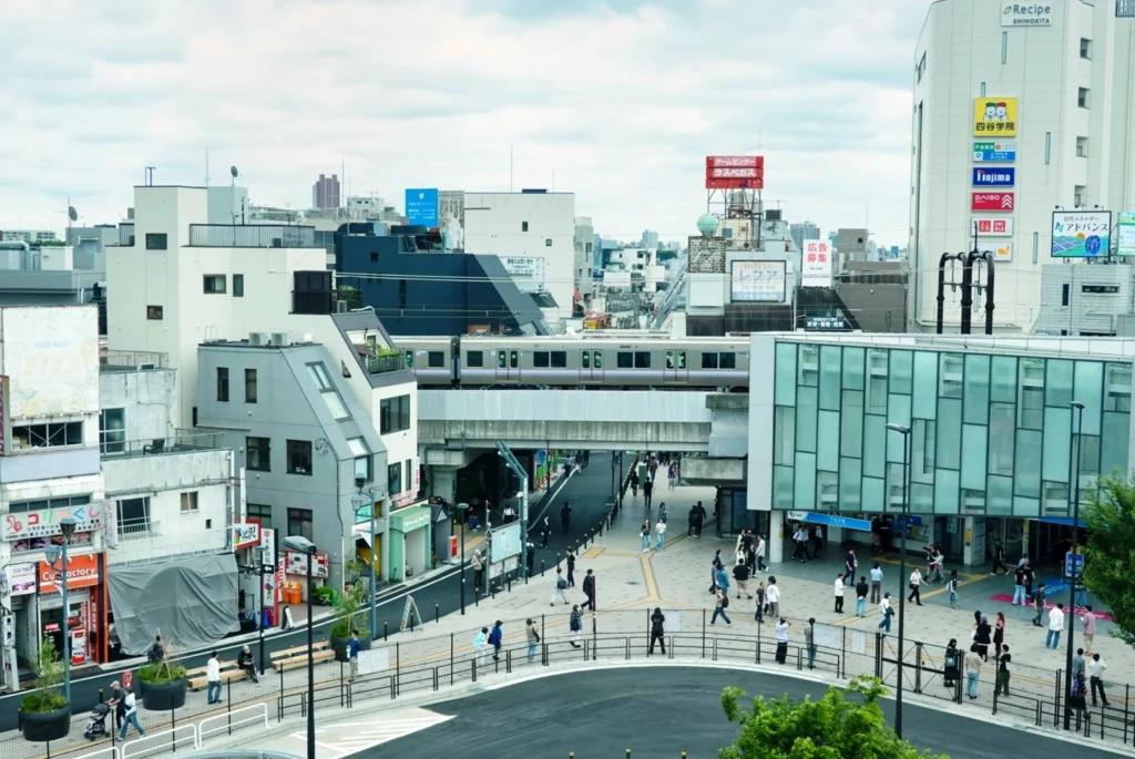 Elevated view of the pedestrian-friendly Shimokitazawa station square with a commuter train passing overhead.