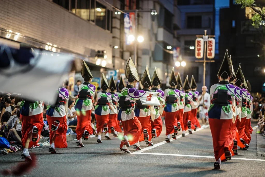 Dancers in colorful traditional costumes and woven straw hats, moving in a synchronized line during the nighttime Tokyo Koenji Awa Odori festival.